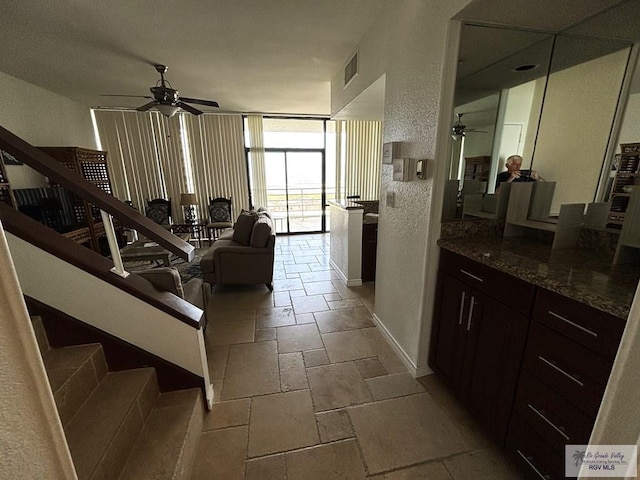 living area with a ceiling fan, stone tile floors, floor to ceiling windows, visible vents, and a textured wall