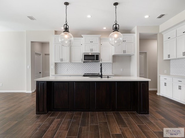 23756 Richmond Cir, Harlingen, TX 78552 - kitchen featuring stainless steel microwave, light countertops, decorative backsplash, an island with sink, and dark wood-style floors