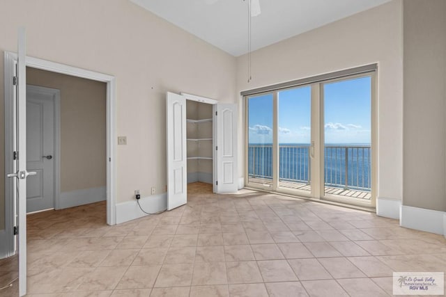 201 W Capricorn Dr, South Padre Island, TX 78597 - unfurnished bedroom featuring access to exterior, light tile patterned floors, a water view, a towering ceiling, and a ceiling fan