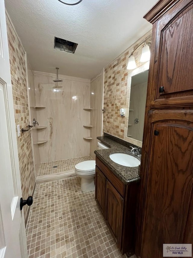 bathroom with a textured ceiling, vanity, tiled shower, and tile walls