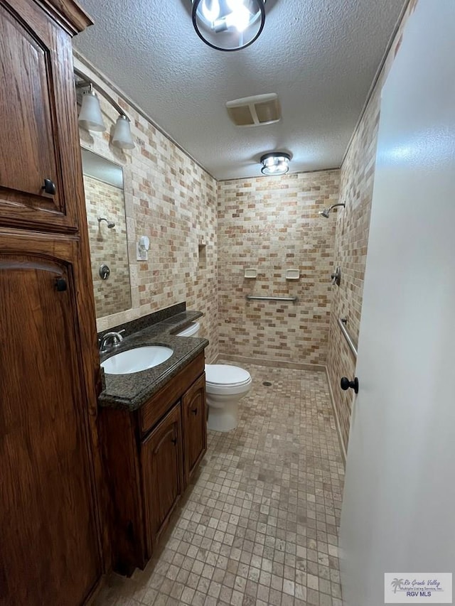 bathroom featuring vanity, toilet, a textured ceiling, tiled shower, and tile walls