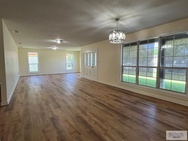 empty room featuring a textured ceiling, dark hardwood / wood-style floors, and an inviting chandelier