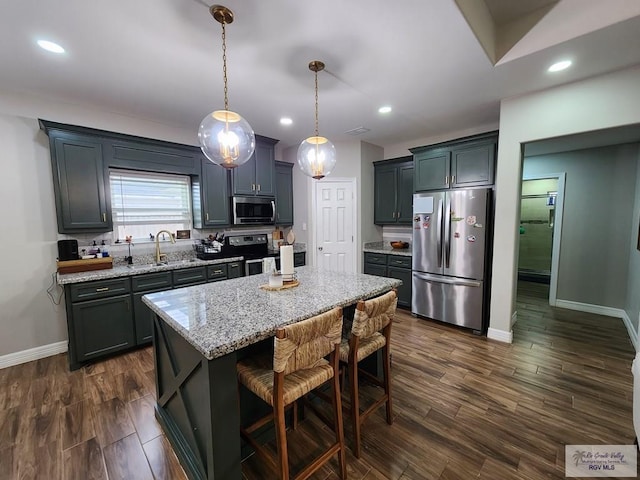 kitchen with a breakfast bar area, light stone counters, a center island, hanging light fixtures, and stainless steel appliances