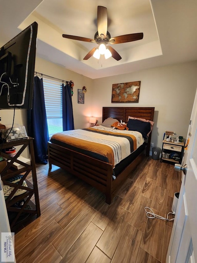 bedroom with hardwood / wood-style floors, ceiling fan, and a tray ceiling