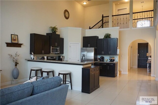 kitchen with stainless steel appliances, kitchen peninsula, a towering ceiling, stone countertops, and light tile patterned floors