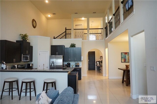 kitchen featuring kitchen peninsula, a towering ceiling, stainless steel appliances, and light tile patterned floors