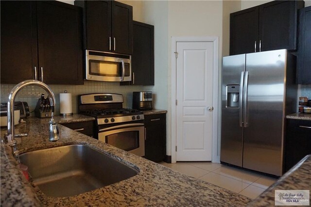 kitchen with sink, stainless steel appliances, backsplash, stone countertops, and light tile patterned floors