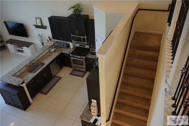 kitchen with sink, light tile patterned floors, stone countertops, and appliances with stainless steel finishes