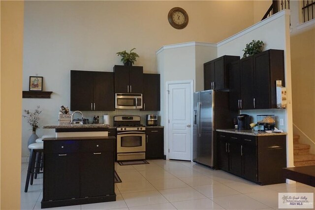 kitchen with decorative backsplash, appliances with stainless steel finishes, sink, light tile patterned floors, and a high ceiling