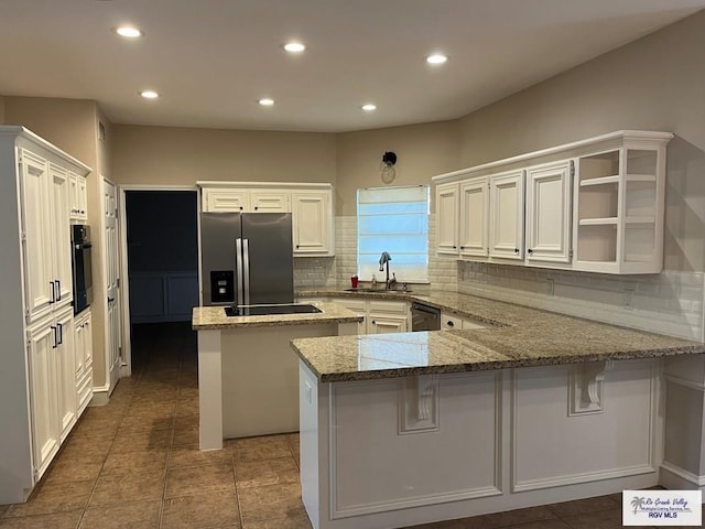 901 Morelos Ave, Rancho Viejo, TX 78575 - kitchen with black appliances, a peninsula, light stone counters, backsplash, and recessed lighting