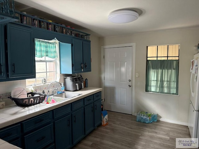 kitchen featuring tile counters, wood finished floors, blue cabinets, and a sink