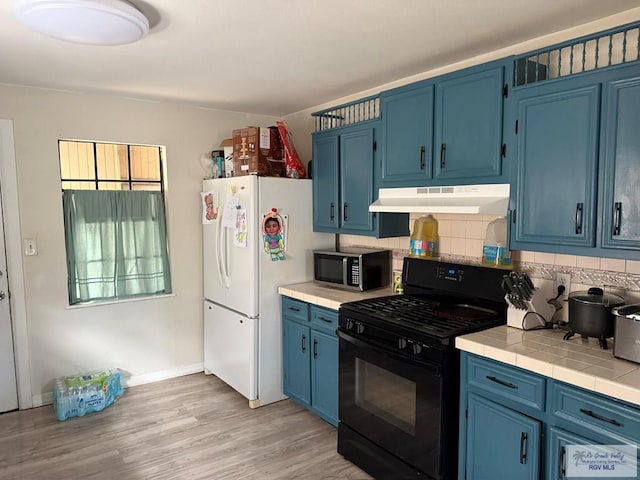 kitchen with tile countertops, blue cabinetry, black range with gas cooktop, under cabinet range hood, and stainless steel microwave