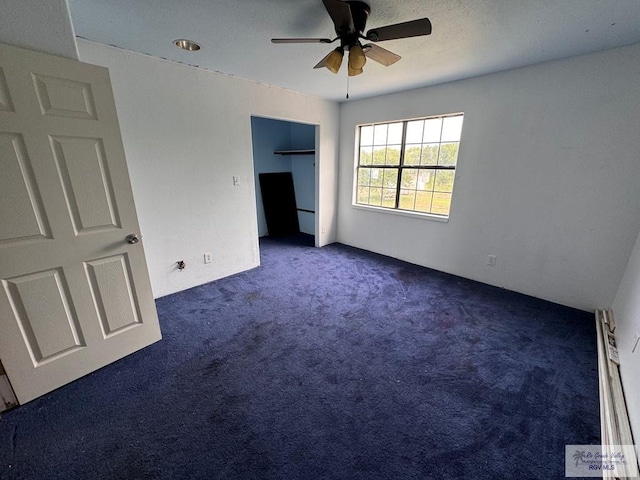 unfurnished bedroom featuring ceiling fan, dark carpet, and a baseboard heating unit