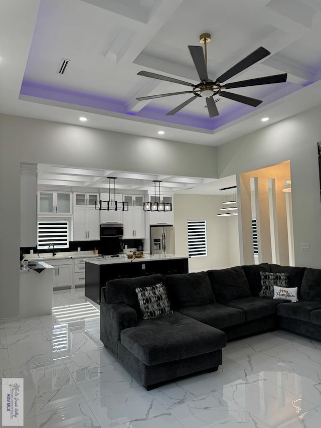 living room featuring a tray ceiling, ceiling fan, and sink