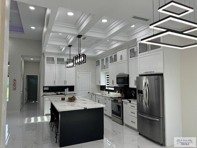 kitchen with light stone countertops, stainless steel appliances, pendant lighting, white cabinets, and a center island