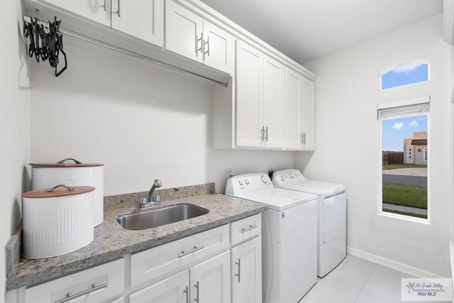 laundry room with a sink, cabinet space, light tile patterned floors, baseboards, and washing machine and clothes dryer