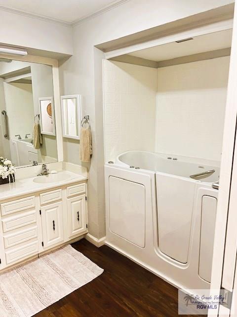 bathroom featuring wood-type flooring, vanity, a tub to relax in, and ornamental molding