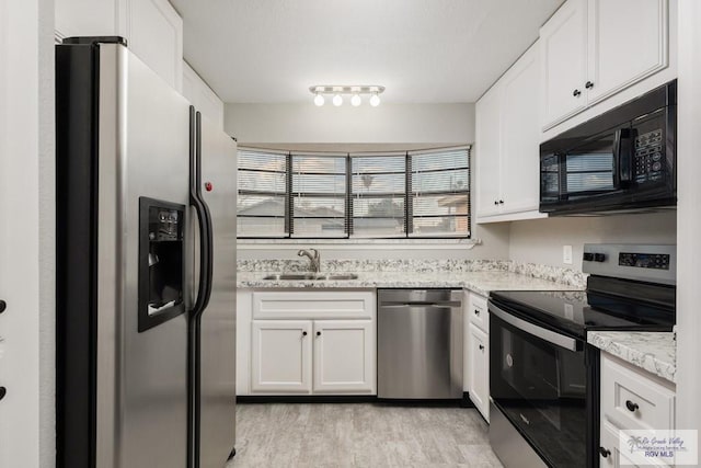 kitchen featuring white cabinets, sink, light hardwood / wood-style flooring, light stone counters, and stainless steel appliances