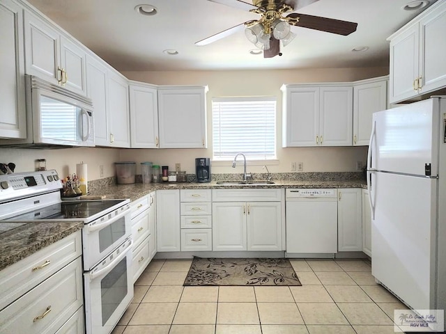 kitchen with white appliances, sink, dark stone countertops, light tile patterned floors, and white cabinetry