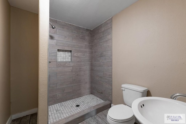 bathroom with tiled shower, sink, and toilet