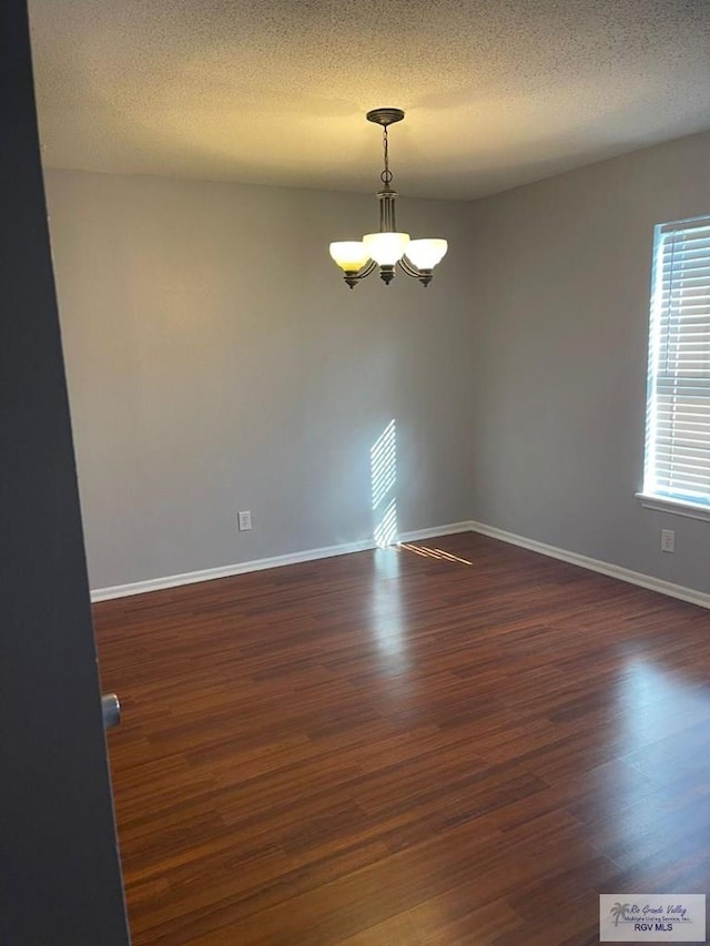 empty room featuring a textured ceiling, a chandelier, and dark hardwood / wood-style floors