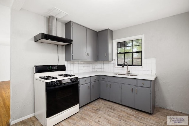 kitchen with gray cabinetry, backsplash, sink, and white stove