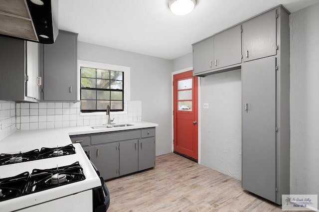 kitchen featuring tasteful backsplash, white gas range, gray cabinetry, sink, and light hardwood / wood-style floors