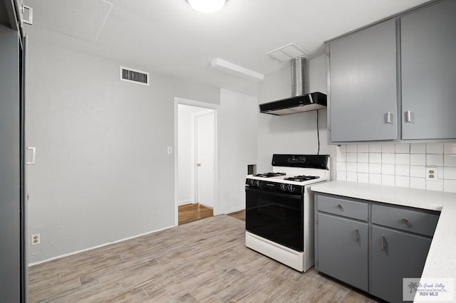 kitchen with backsplash, white range, wall chimney range hood, gray cabinets, and light hardwood / wood-style floors