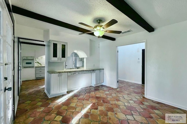 kitchen featuring oven, ceiling fan, a textured ceiling, beamed ceiling, and white cabinetry