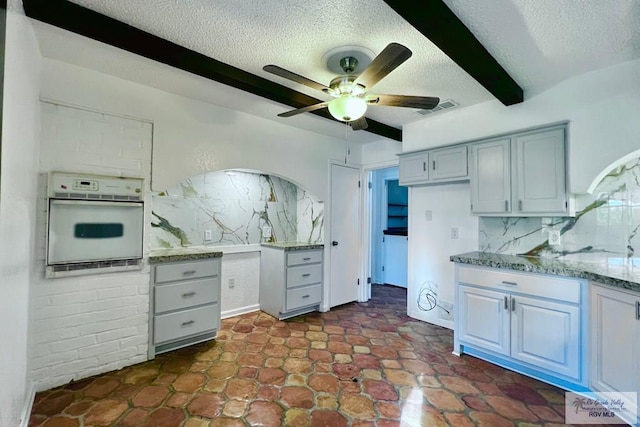 kitchen featuring oven, beam ceiling, ceiling fan, and tasteful backsplash