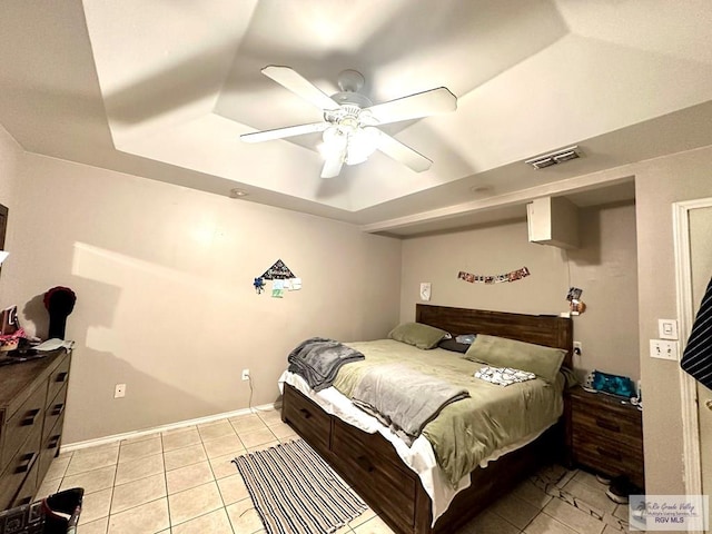 bedroom with visible vents, baseboards, light tile patterned floors, a raised ceiling, and a ceiling fan