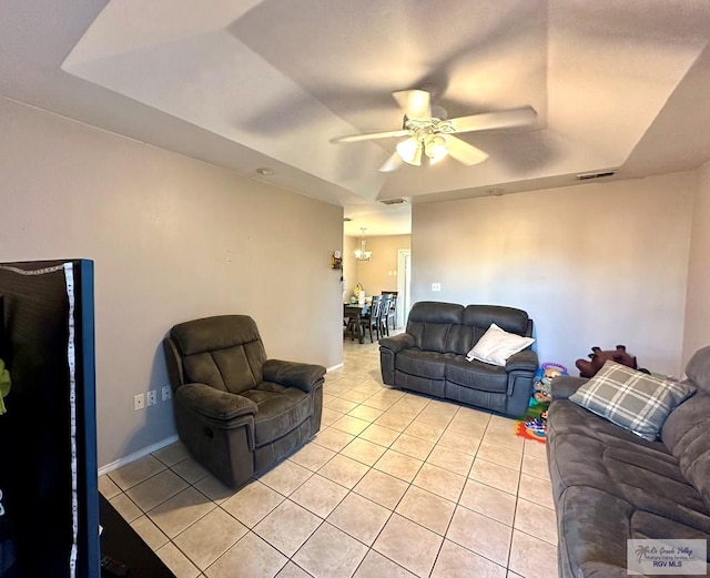 living area with a tray ceiling, light tile patterned flooring, visible vents, and ceiling fan