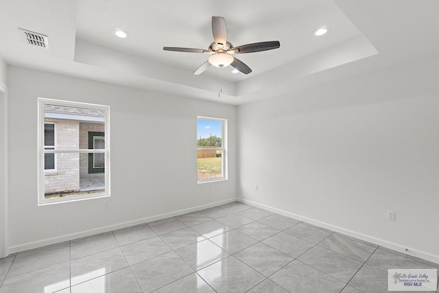 tiled empty room with a raised ceiling and ceiling fan