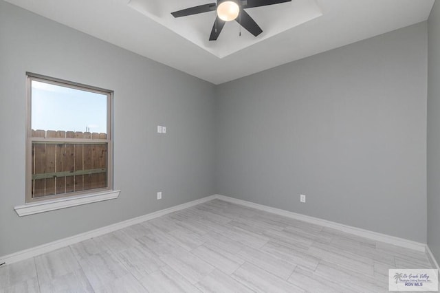 empty room with ceiling fan and a tray ceiling