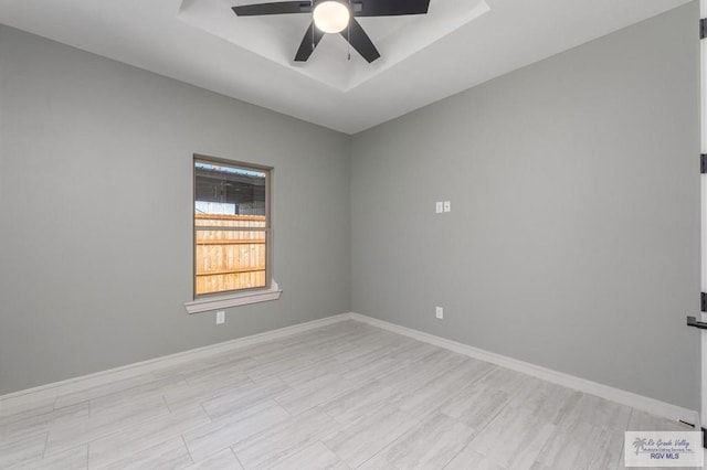 unfurnished room with ceiling fan and a tray ceiling