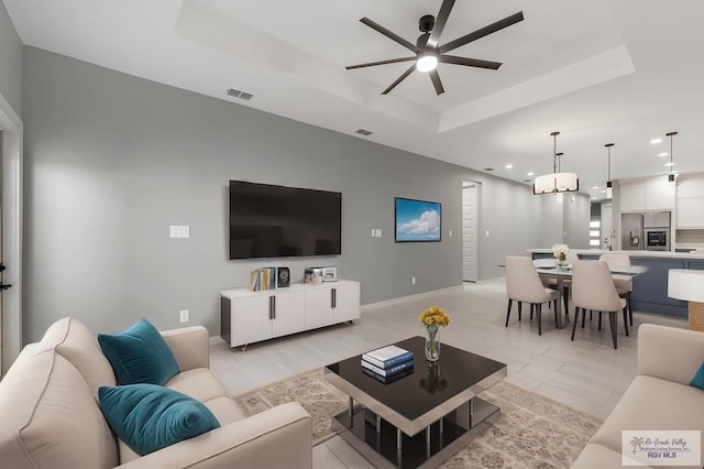 living room featuring ceiling fan, a tray ceiling, sink, and light wood-type flooring