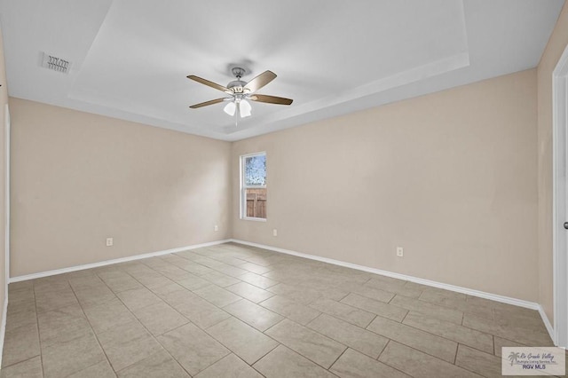 empty room featuring a tray ceiling, ceiling fan, and light tile patterned flooring