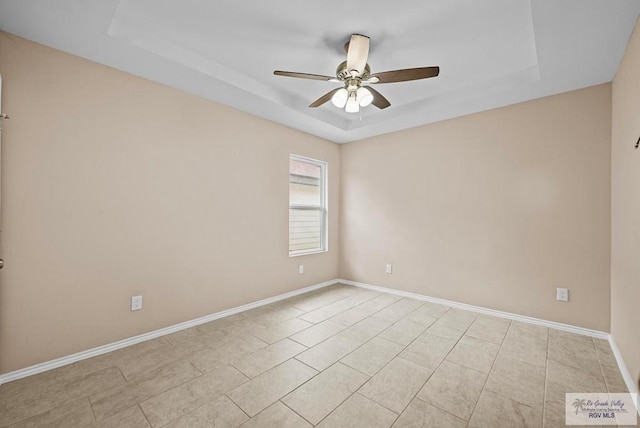 tiled empty room with ceiling fan and a tray ceiling