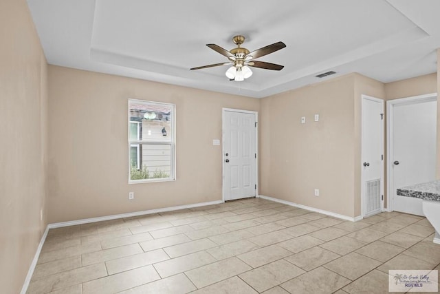 tiled spare room featuring a raised ceiling and ceiling fan