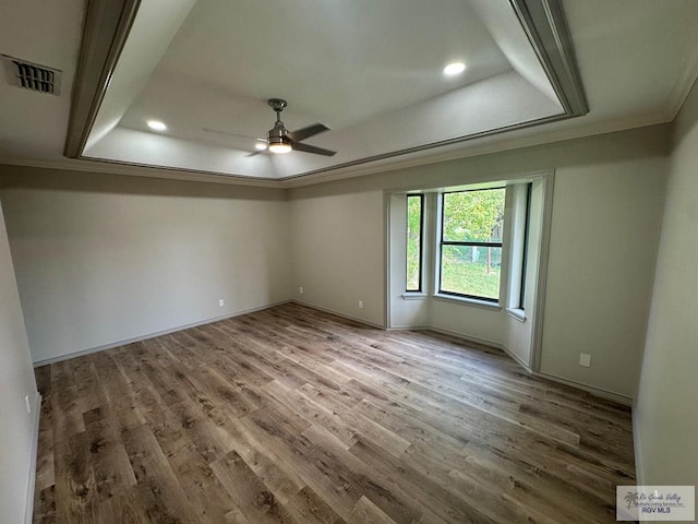 empty room featuring hardwood / wood-style flooring, ceiling fan, ornamental molding, and a tray ceiling