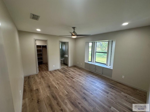 unfurnished bedroom with a spacious closet, ceiling fan, ensuite bathroom, a closet, and hardwood / wood-style flooring