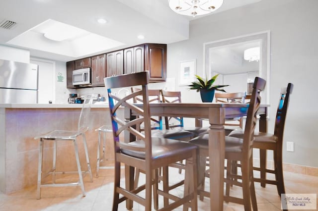 tiled dining room with a tray ceiling and a chandelier