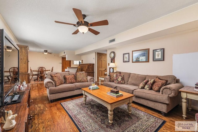 living room featuring hardwood / wood-style flooring, ceiling fan, and a textured ceiling