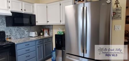 kitchen with tasteful backsplash, light stone counters, ventilation hood, white cabinets, and black appliances