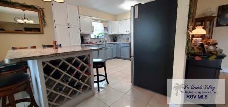 kitchen with white cabinetry, a kitchen breakfast bar, kitchen peninsula, gray cabinets, and light tile patterned floors