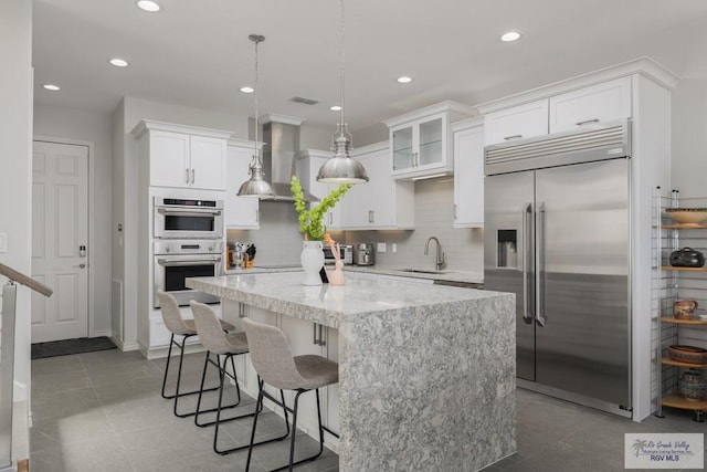 kitchen featuring white cabinets, wall chimney exhaust hood, a kitchen island, appliances with stainless steel finishes, and a sink