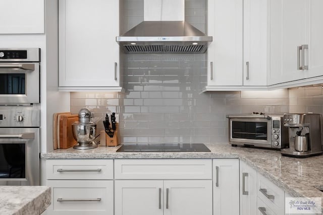 kitchen with white cabinets, decorative backsplash, wall chimney exhaust hood, black electric cooktop, and stainless steel double oven