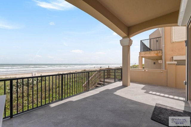 view of patio / terrace featuring a water view, a beach view, and a balcony