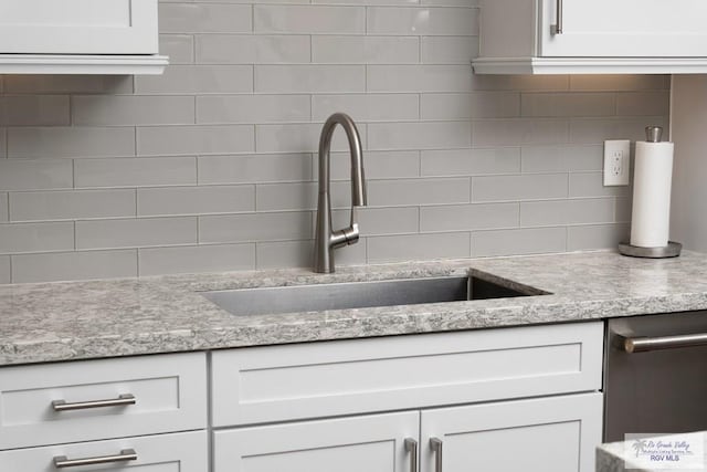 kitchen featuring a sink, light stone countertops, white cabinets, and backsplash