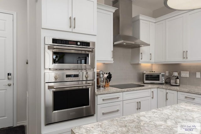 kitchen featuring white cabinets, black electric stovetop, stainless steel double oven, wall chimney range hood, and backsplash